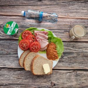 Zdjęcie przedstawia: Dietę z ograniczeniem łatwoprzyswajalnych węglowodanów  Chleb Graham Masło extra Pomidor Kefir Szynka krucha z pieca wieprzowa, parzona Woda mineralna Sałata zielona Hummus paprykowy